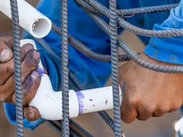 Technician fitting a PVC irrigation pipe to rebar on a construction site